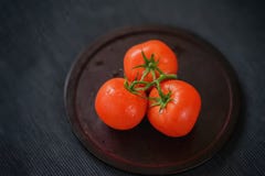 Trois tomates mûres rouges fraîches avec de l'eau se laisse tomber sur des branches, plat en bois, fond noir Foyer sélectif Vue s Photographie stock Trois tomates mûres rouges fraîches avec de l'eau se laisse tomber sur des branches, plat en bois, fond noir Foyer sélectif Vue s Photographie stock