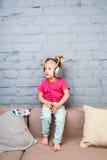 Troszkę siedzi na leżance śmieszna dziewczyna dwa roku, słucha muzyka na hełmofonach stawiających na jej głowie Trzyma smartphone obrazy royalty free Troszkę siedzi na leżance śmieszna dziewczyna dwa roku, słucha muzyka na hełmofonach stawiających na jej głowie Trzyma smartphone obrazy royalty free