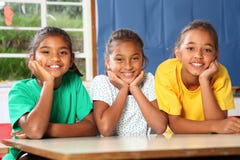 Três meninas novas felizes da escola que inclinam-se na mesa dentro fotografia de stock royalty free Três meninas novas felizes da escola que inclinam-se na mesa dentro fotografia de stock royalty free