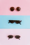 Três óculos de sol em um rosa e em um fundo pastel azul O conceito do verão e de férias à moda fotos de stock Três óculos de sol em um rosa e em um fundo pastel azul O conceito do verão e de férias à moda fotos de stock