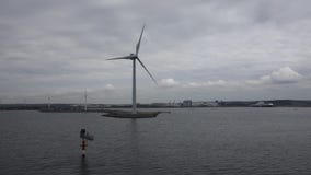 Turbinas de viento a lo largo de la orilla vista del agua Turbinas de viento a lo largo de la orilla vista del agua