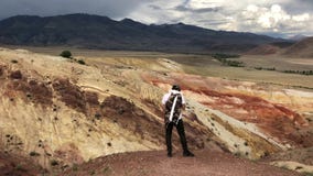 Turista masculino joven que admira las montañas hermosas montañas rojas hermosas de Altai Reserva natural de la montaña Altai almacen de metraje de vídeo Turista masculino joven que admira las montañas hermosas montañas rojas hermosas de Altai Reserva natural de la montaña Altai almacen de metraje de vídeo
