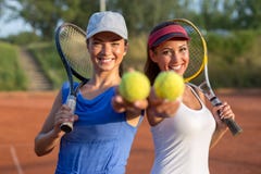 Två härliga unga kvinnor som rymmer tennisutrustning in i kameran royaltyfri bild Två härliga unga kvinnor som rymmer tennisutrustning in i kameran royaltyfri bild