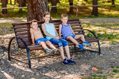 Två pojkar och en flicka som sitter på en bänk i sommaren barn tre royaltyfri foto Två pojkar och en flicka som sitter på en bänk i sommaren barn tre royaltyfri foto
