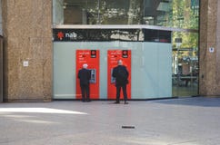 Twee bedrijfsmens in zwarte kostuums die DUTJEatm uit kant gebruiken het gebouw in Sydney stock foto's Twee bedrijfsmens in zwarte kostuums die DUTJEatm uit kant gebruiken het gebouw in Sydney stock foto's