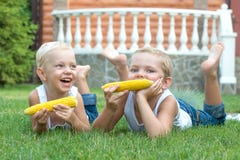 Twee broers die op het gras liggen en eten maïskolven in de tuin stock foto Twee broers die op het gras liggen en eten maïskolven in de tuin stock foto