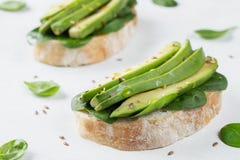 Twee ciabattatoost met gesneden avocadoolijfolie, spinazie en vlas en sesamzaden Gezond vegetarisch Ontbijt stock fotografie Twee ciabattatoost met gesneden avocadoolijfolie, spinazie en vlas en sesamzaden Gezond vegetarisch Ontbijt stock fotografie