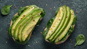 Twee ciabattatoost met gesneden avocadoolijfolie, spinazie en vlas en sesamzaden Gezond vegetarisch Ontbijt op dark stock foto Twee ciabattatoost met gesneden avocadoolijfolie, spinazie en vlas en sesamzaden Gezond vegetarisch Ontbijt op dark stock foto