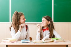 Twee donkerbruine schoolmeisjes zitten in het klaslokaal bij haar bureau met boeken op de achtergrond van het bord royalty-vrije stock afbeelding Twee donkerbruine schoolmeisjes zitten in het klaslokaal bij haar bureau met boeken op de achtergrond van het bord royalty-vrije stock afbeelding