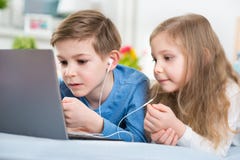 Twee gelukkige kinderen die met laptop en het luisteren muziek spelen met royalty-vrije stock afbeeldingen Twee gelukkige kinderen die met laptop en het luisteren muziek spelen met royalty-vrije stock afbeeldingen