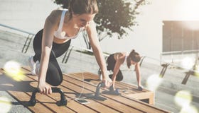Twee jonge glimlachende vrouwen, meisjes in sportkleding het doen oefent terwijl het luisteren aan muziek uit Training, die op st stock afbeelding Twee jonge glimlachende vrouwen, meisjes in sportkleding het doen oefent terwijl het luisteren aan muziek uit Training, die op st stock afbeelding