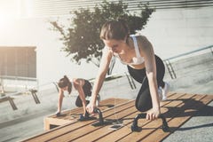 Twee jonge glimlachende vrouwen, meisjes in sportkleding het doen oefent terwijl het luisteren aan muziek uit Training, die op st stock afbeelding Twee jonge glimlachende vrouwen, meisjes in sportkleding het doen oefent terwijl het luisteren aan muziek uit Training, die op st stock afbeelding