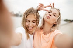 Twee jonge mooie blondemeisjes nemen een selfie op het strand op een warme winderige dag stock fotografie Twee jonge mooie blondemeisjes nemen een selfie op het strand op een warme winderige dag stock fotografie