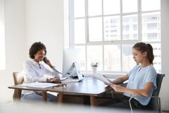 Twee jonge vrouwen aan het werk, aangaande de telefoon en lezingsdocumenten stock afbeeldingen Twee jonge vrouwen aan het werk, aangaande de telefoon en lezingsdocumenten stock afbeeldingen