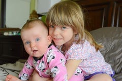 Twee kleine aanbiddelijke Kaukasische zusters zitten samen De kleine zuster koestert haar baby-zuster De meisjes glimlachen en ge stock afbeeldingen Twee kleine aanbiddelijke Kaukasische zusters zitten samen De kleine zuster koestert haar baby-zuster De meisjes glimlachen en ge stock afbeeldingen
