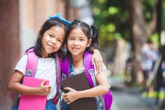 Twee leuke Aziatische kindmeisjes die met schooltas een boek samen in de school houden royalty-vrije stock foto Twee leuke Aziatische kindmeisjes die met schooltas een boek samen in de school houden royalty-vrije stock foto