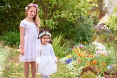 Twee meisjes in witte kleding en bloemkroon die pret hebben een de zomertuin royalty-vrije stock afbeelding Twee meisjes in witte kleding en bloemkroon die pret hebben een de zomertuin royalty-vrije stock afbeelding