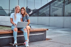 Twee mooie meisjes die houdt laptop en het bekijken een camera terwijl het zitten op de bank op achtergrond van zitten stock fotografie Twee mooie meisjes die houdt laptop en het bekijken een camera terwijl het zitten op de bank op achtergrond van zitten stock fotografie
