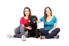 Twee vrouwelijke vrienden die op een vloer zitten en met een hond stellen stock afbeelding Twee vrouwelijke vrienden die op een vloer zitten en met een hond stellen stock afbeelding