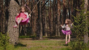 Two girls are swinging on swings in the forest stock video Two girls are swinging on swings in the forest stock video