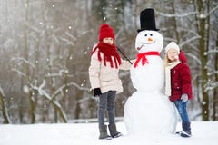 Two adorable little girls building a snowman together in beautiful winter park. Cute sisters playing in a snow. Royalty Free Stock Photos Two adorable little girls building a snowman together in beautiful winter park. Cute sisters playing in a snow. Royalty Free Stock Photos