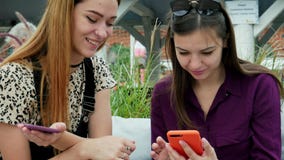 Two attractive young women using mobile phones and talking. Friends enjoying good time at terrace stock video Two attractive young women using mobile phones and talking. Friends enjoying good time at terrace stock video