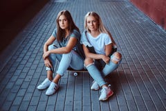 Two beautiful hipster girls sitting on a skateboard at a sidewalk under bridge. royalty free stock image Two beautiful hipster girls sitting on a skateboard at a sidewalk under bridge. royalty free stock image