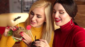 Two beautiful young girls with bright make-up eat burgers in a cafe. stock video footage Two beautiful young girls with bright make-up eat burgers in a cafe. stock video footage