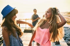 Two beautiful young girls having fun at the evening seaside with group of their friends on background stock photography Two beautiful young girls having fun at the evening seaside with group of their friends on background stock photography