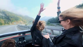 Two beautiful young girls ride in a red cabriolet among the mountains. Road on the highway. Dressed in black leather stock footage Two beautiful young girls ride in a red cabriolet among the mountains. Road on the highway. Dressed in black leather stock footage