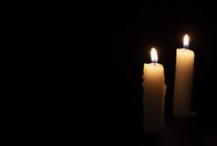 Two candles on black background. Lighting candles in darkness. Yellow wax candle with warm flame. In memoriam banner