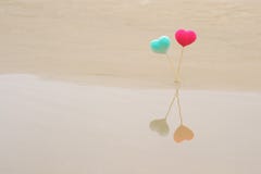 Two crocheted bright and colorful hearts on wooden sticks on beach, reflected in water. Pink red and blue turquoise hearts. royalty free stock photo Two crocheted bright and colorful hearts on wooden sticks on beach, reflected in water. Pink red and blue turquoise hearts. royalty free stock photo