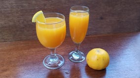 two glass of fresh orange juice and one orange fruit on the brown wooden table stock photo two glass of fresh orange juice and one orange fruit on the brown wooden table stock photo