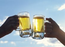 Two glasses of light beer hold male hands against the blue sky. Friends toasting with wheat beer stock photos Two glasses of light beer hold male hands against the blue sky. Friends toasting with wheat beer stock photos