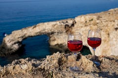 Two glasses of rose dry white wine served on rocks in blue sea bay with Love Bridge on background near Ayia Napa touristic town on