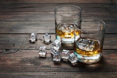 Two glasses of whiskey with ice cubes served on wooden planks. Vintage countertop and a glass of hard liquor Royalty Free Stock Photography Two glasses of whiskey with ice cubes served on wooden planks. Vintage countertop and a glass of hard liquor Royalty Free Stock Photography