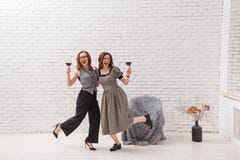 Two happy women, having fun and drinking red wine on party. Fashionable dressed with beautiful wavy hair. On loft white stock photo Two happy women, having fun and drinking red wine on party. Fashionable dressed with beautiful wavy hair. On loft white stock photo