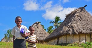 Two male young children in Navala, Fiji smiling looking into the camera with traditional Fijian home bure behind