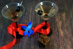 Two martini glasses with olives, with scarlet ribbon, blue orchid and gift box on a wooden table stock photos Two martini glasses with olives, with scarlet ribbon, blue orchid and gift box on a wooden table stock photos