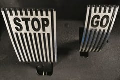 Two metal pedals of an electric car in gray with the words STOP and GO close-up.