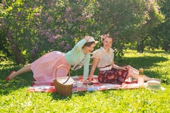Two pretty girls friends sitting on the red blanket on the green grass and have summer picnic. happy woman having rest and fun on royalty free stock photo Two pretty girls friends sitting on the red blanket on the green grass and have summer picnic. happy woman having rest and fun on royalty free stock photo