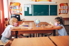Two Schoolgirls In Medical Masks Are Sitting At A School Desk, Opposite Each Other, Group Session, Back To School, Teaching Royalty Free Stock Photo