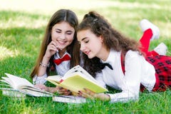 Two schoolgirls in school uniforms sit with books in the park. Schoolgirls or students are taught lessons in nature