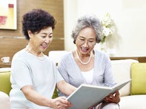 Two senior asian women reading a book together stock photo Two senior asian women reading a book together stock photo