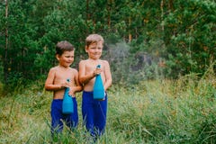 Two tanned boys in blue pants splash water from sprayers in the green forest. In the summer Royalty Free Stock Image Two tanned boys in blue pants splash water from sprayers in the green forest. In the summer Royalty Free Stock Image