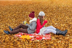 Two teenage girl and boy sitting in the park on a plaid backs to each other and keep warm drinking tea royalty free stock image Two teenage girl and boy sitting in the park on a plaid backs to each other and keep warm drinking tea royalty free stock image