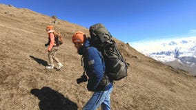 Two tourists photographers with backpacks in hats and sunglasses go up the hill on the yellow grass with cameras in stock footage Two tourists photographers with backpacks in hats and sunglasses go up the hill on the yellow grass with cameras in stock footage