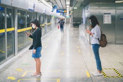 Two young asian woman wearing protective face mask stand in line with social distancing during waiting train in subway due to