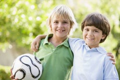Two young boys outdoors with soccer ball smiling