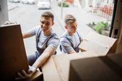 Two young handsome smiling movers wearing uniforms are unloading the van full of boxes. House move, mover service royalty free stock photo Two young handsome smiling movers wearing uniforms are unloading the van full of boxes. House move, mover service royalty free stock photo